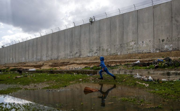 TOPSHOT - A picture taken on February 14, 2018 shows a Palestinian boy running between water puddles and Israel's controversial separation barrier in the occupied West Bank town of Qalqilyah. (Photo by Jaafar ASHTIYEH / AFP) (Photo by JAAFAR ASHTIYEH/AFP via Getty Images)